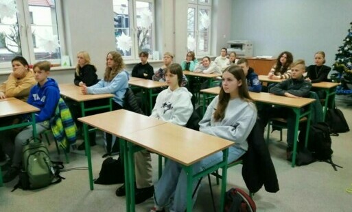 Zdjęcie grupowe młodzieży i dwóch opiekunek na tle klasy szkolnej.